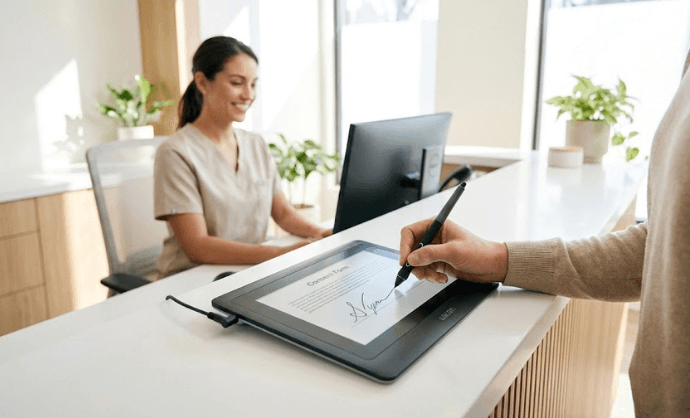 Paciente firmando consentimiento en una tablet para firmar documentos sobre el mostrador de una clínica, con captura biométrica de la firma